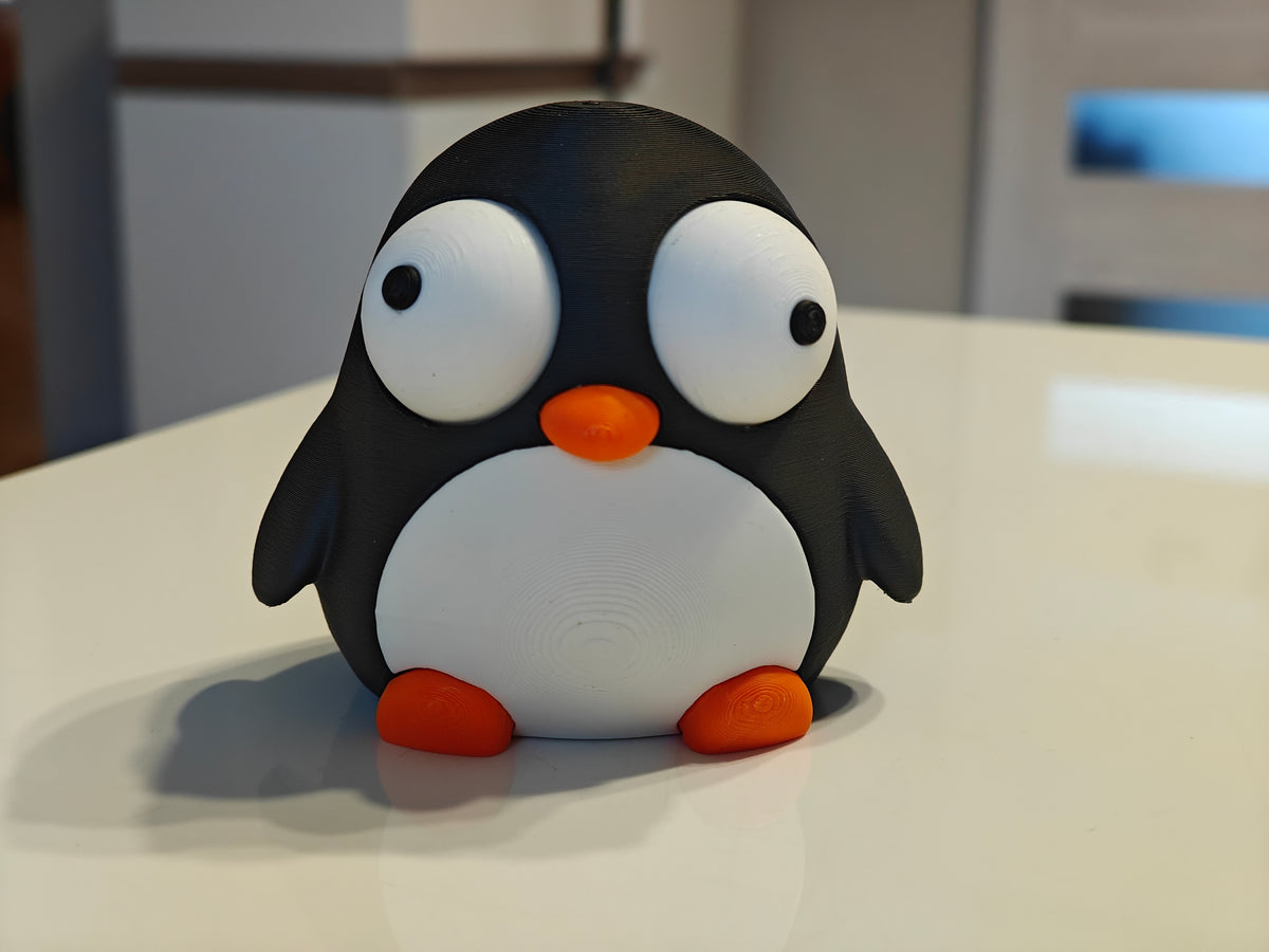 Petite figurine pingouin aux yeux mobiles sur un bureau près d'une tasse à café