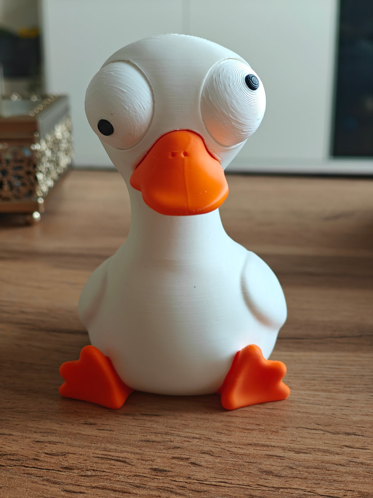 Petite figurine d'oie aux yeux mobiles sur une étagère en bois près d'une plante