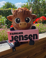 Panneau de bienvenue avec nom de famille – vache Highland tenant une pancarte « Familien Jensen »