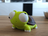Figurine de tortue rigolote aux yeux mobiles sur un bureau près d'une plante