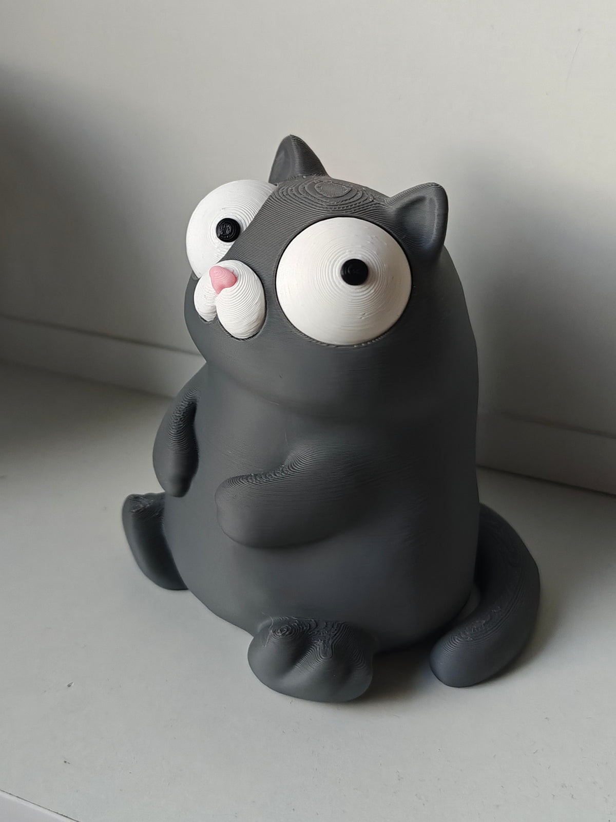 Figurine de chat rigolote aux yeux mobiles sur un bureau près d'un mug
