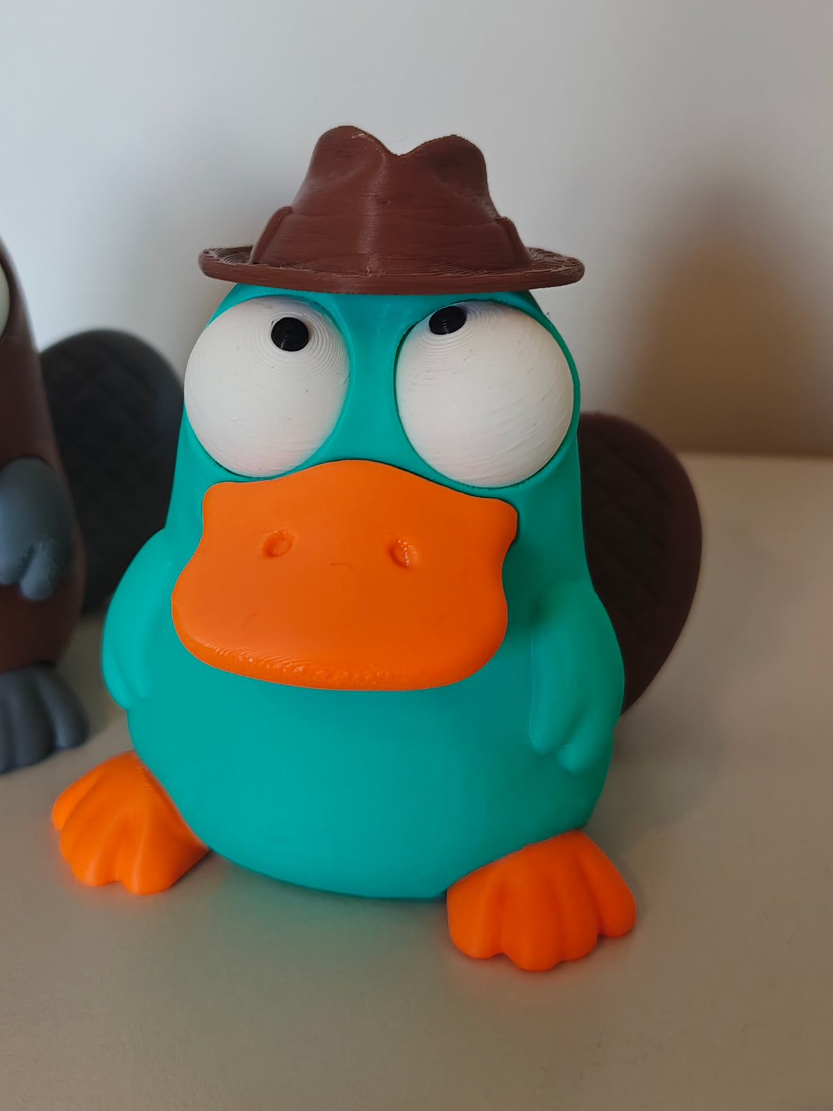 Figurine d'ornithorynque aux yeux mobiles sur un bureau en bois à côté d'une tasse de café