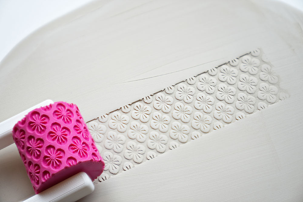Rouleau à texture avec poignée pour céramique sur une surface blanche avec détail du motif