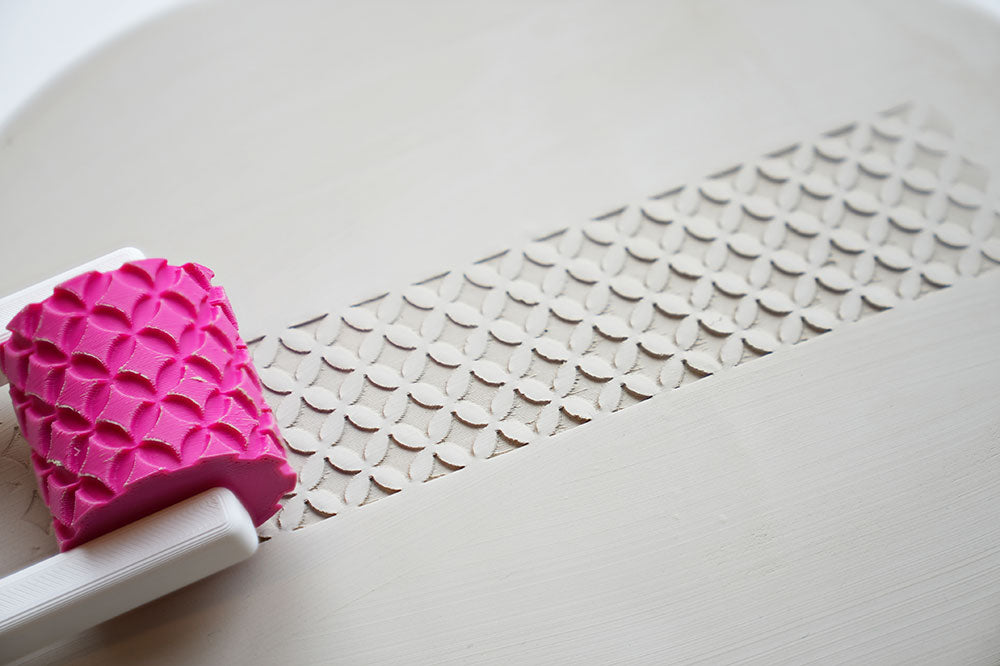 Rouleau à texture avec poignée pour céramique sur une surface blanche avec détail du motif