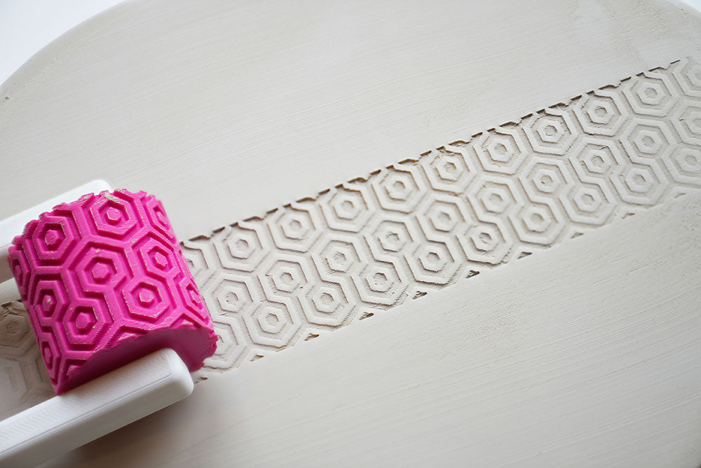 Rouleau à texture avec poignée pour céramique sur une surface blanche avec détail du motif