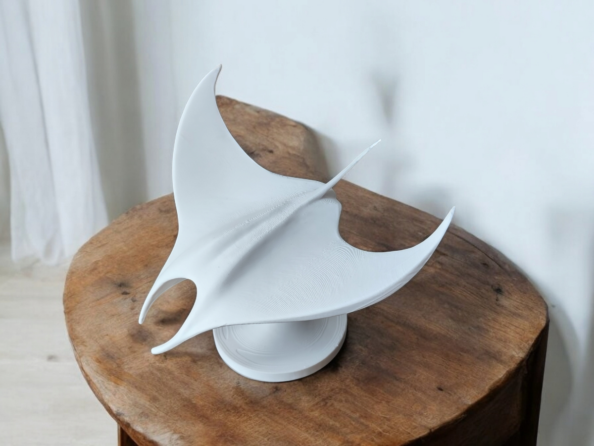 Sculpture minimaliste d'une raie manta sur une étagère en bois clair contre un mur blanc
