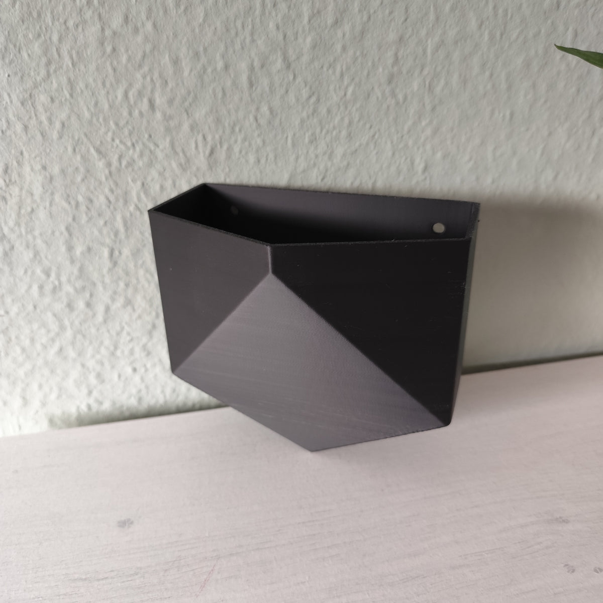 Pot mural low poly fixé sur un mur blanc avec une petite plante en pot