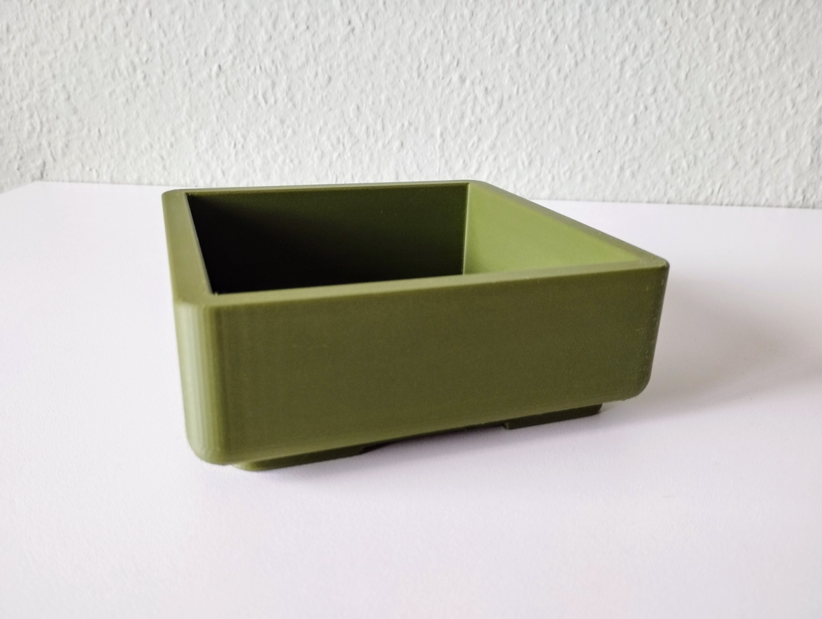 Pot à bonsaï carré sur le rebord de fenêtre avec une petite plante verte