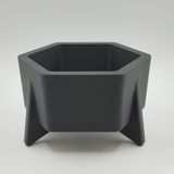 Pot de fleurs hexagonal style mid-century sur une étagère blanche avec petite plante grasse