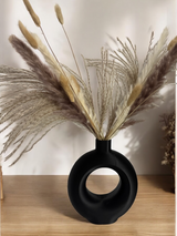 Vase anneau minimaliste avec une seule tige séchée sur une étagère blanche