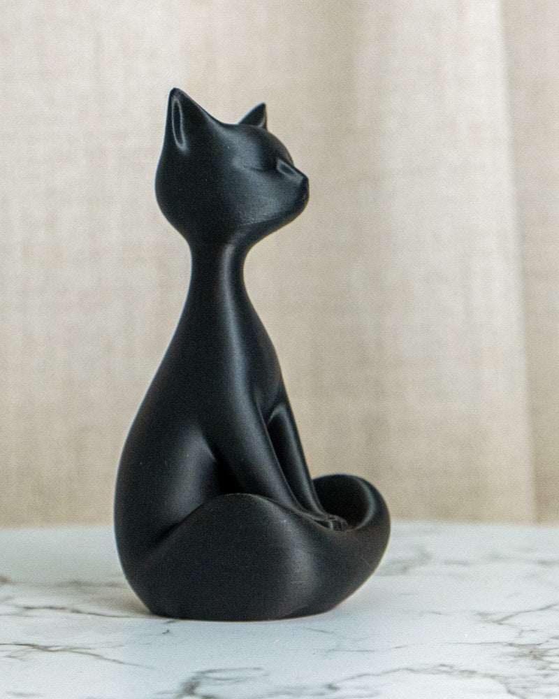 Gros plan d'une sculpture de chat noir mat assis bien droit sur fond blanc