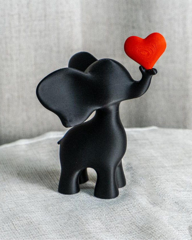 Gros plan d'une sculpture d'éléphant noir avec cœur rouge sur surface blanche