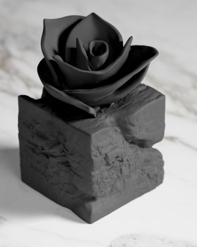 Sculpture de rose noire jaillissant d'un socle en pierre brute, vue de face sur surface blanche