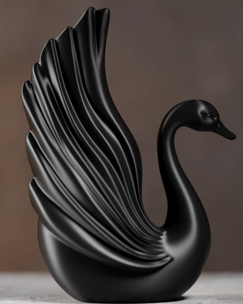 Sculpture de cygne noir au cou courbé et aux ailes levées sur fond blanc
