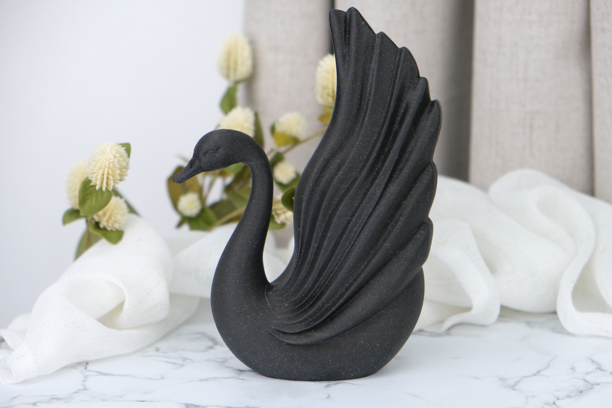 Sculpture de cygne noir sur une étagère minimaliste près de céramiques et d'une bougie