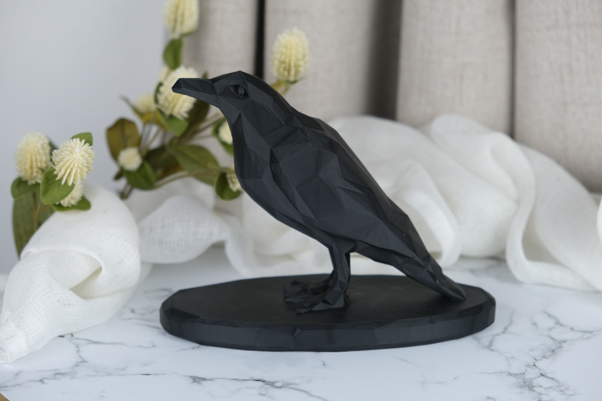 Sculpture de corbeau low poly sur une étagère en bois avec une bougie et une céramique sombre