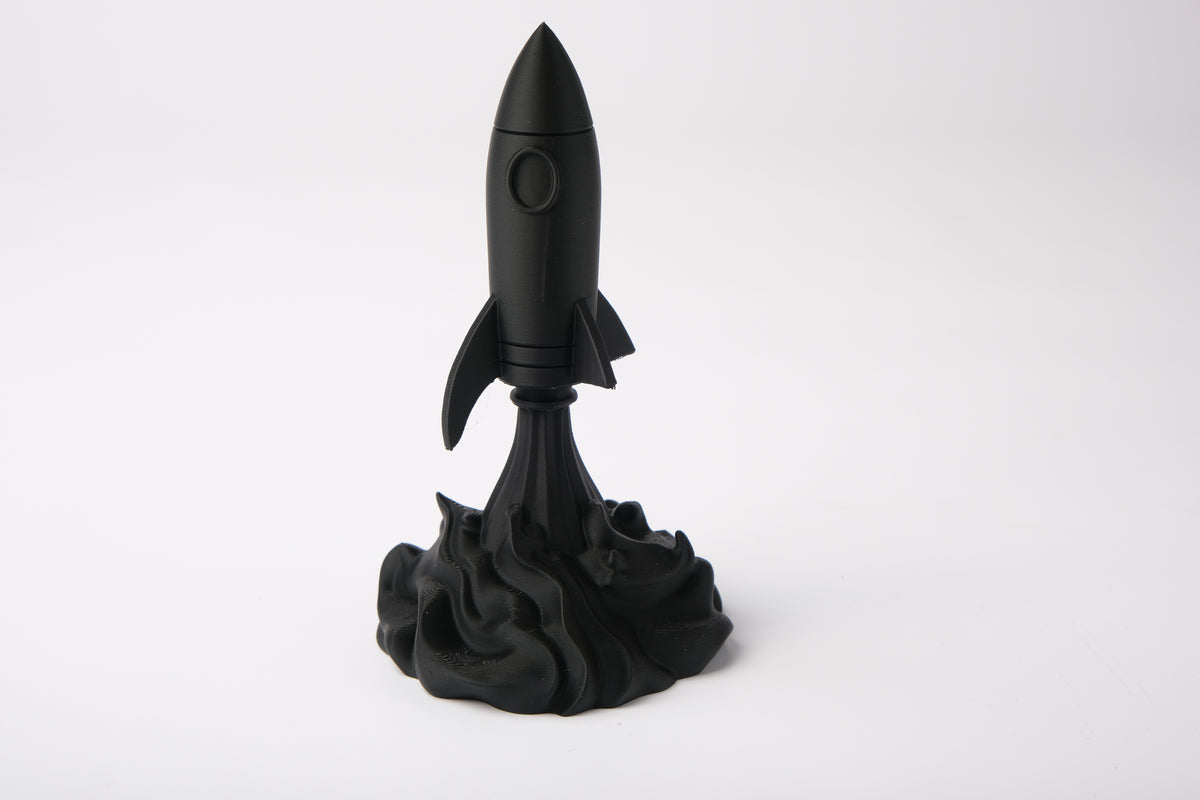 Sculpture de fusée sur un bureau en bois avec des livres et une petite plante, style minimaliste
