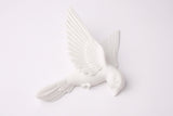 Sculpture murale blanche minimaliste avec des oiseaux sur un mur de salon gris chaud