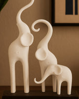Sculpture d'éléphants minimaliste à trois figures stylisées sur socle sombre, fond blanc, gros plan