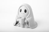 Figurine de fantôme attendrissante sur un bureau en bois près d'une petite plante et de livres sous une lumière chaude