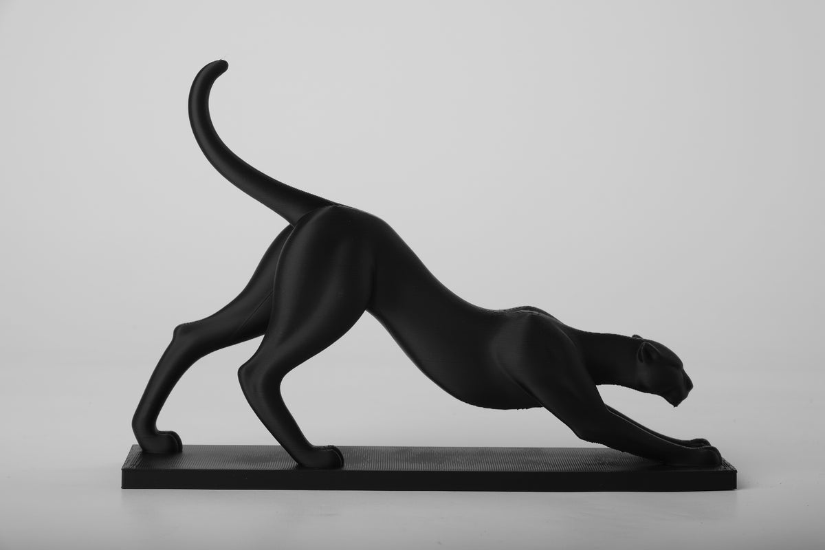 Sculpture d'une panthère qui s'étire sur une étagère en bois avec livres et céramiques