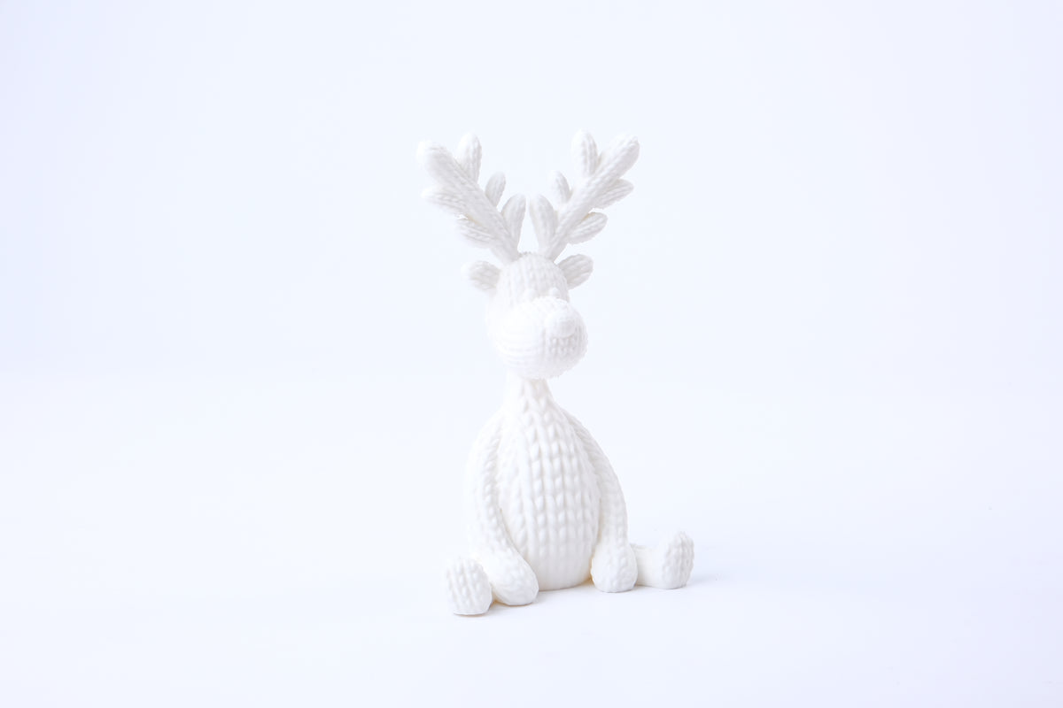 Figurine de renne tricotée sur une étagère avec des bougies et des plantes séchées dans un salon scandinave