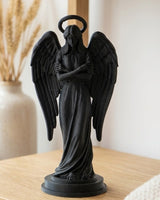 Figurine d'ange noir mat aux ailes déployées sur une surface blanche, gros plan