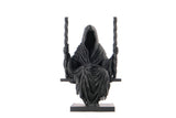 Sculpture gothique sombre de la Faucheuse sur une étagère en bois foncé avec bougies et ambiance lugubre