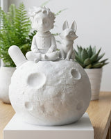 Le Petit Prince sur la Lune avec la figurine du renard sur une surface blanche, vue de face