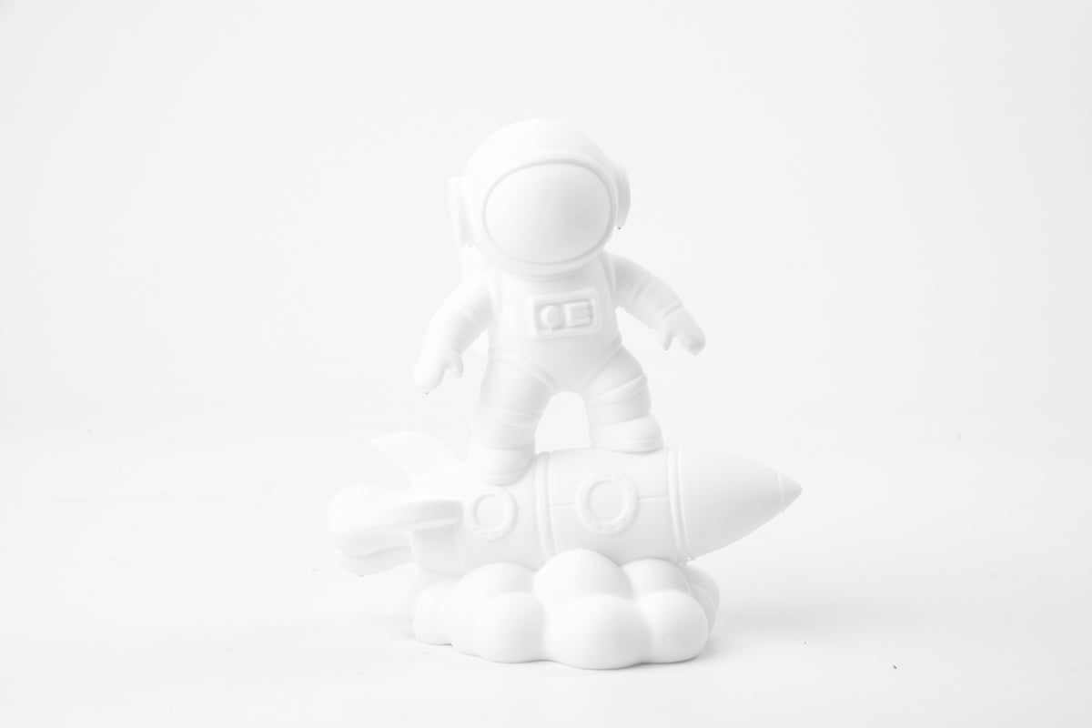 Sculpture d'astronaute sur une fusée sur un bureau minimaliste près d'une plante et de petits livres