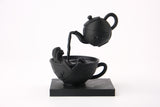 Sculpture Tea Time Reverie sur une étagère sombre avec livres et décoration minimaliste