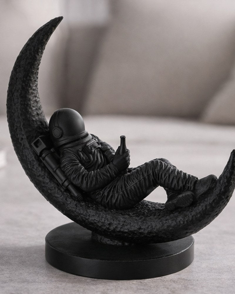 Sculpture d'astronaute assis sur un croissant de lune, finition mate, gros plan sur fond blanc