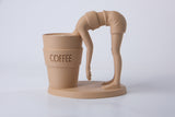 Sculpture surréaliste de café sur un bureau en bois près d'une tasse en céramique et d'une petite plante