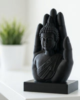 Sculpture de main de Bouddha noir mat sur une surface blanche, avec une figure sereine dans la paume ouverte