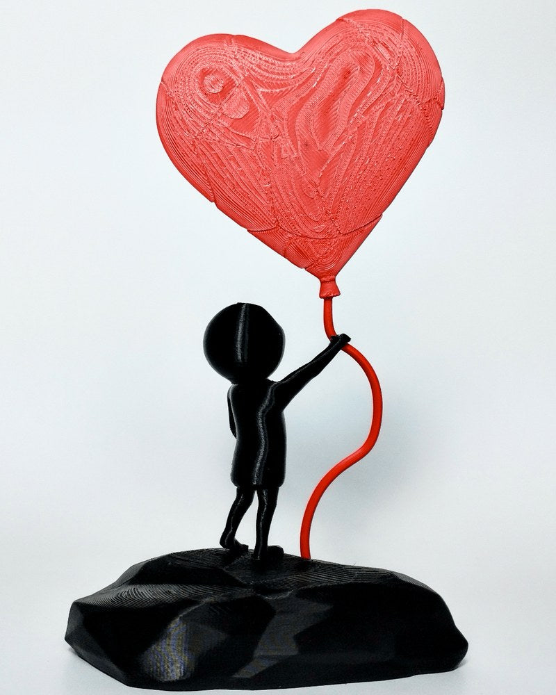 Gros plan d'une sculpture noire de garçon avec ballon cœur rouge sur fond blanc