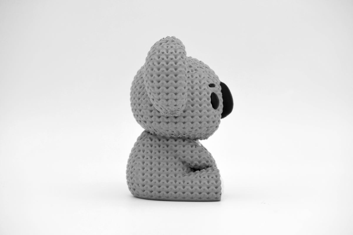 Petit koala façon tricot sur une étagère en bois clair près d'une plante, intérieur scandinave
