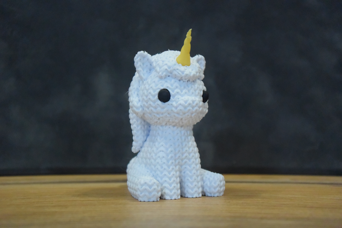 Figurine de licorne tricotée sur une étagère en bois à côté de petites plantes et de détails déco douillets