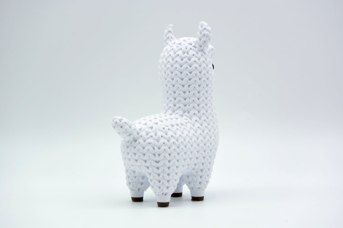 Figurine de lama tricotée sur une étagère en bois à côté d'une petite plante et de livres