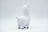 Figurine de lama tricotée sur une étagère en bois à côté d'une petite plante et de livres