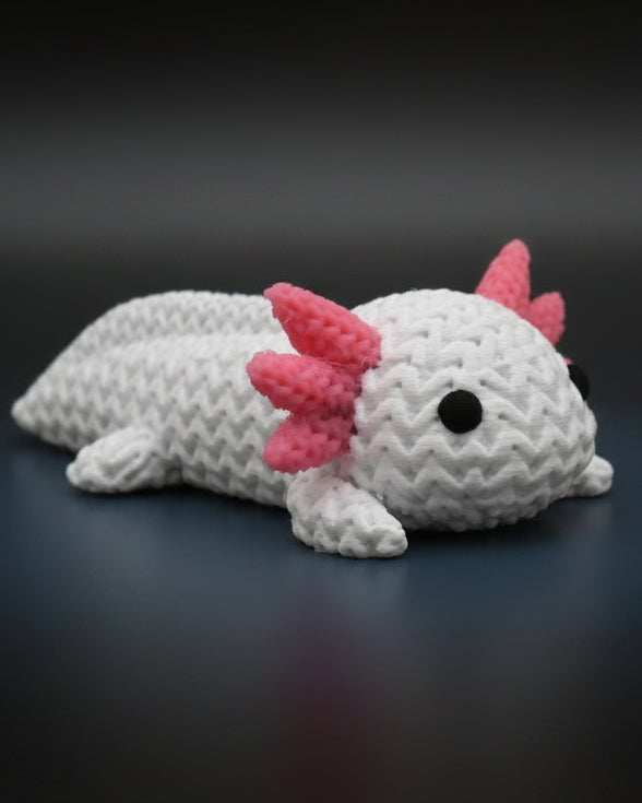 Petit axolotl façon tricot sur une étagère en bois près de livres et d'une plante, décor scandinave