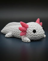 Petit axolotl façon tricot sur une étagère en bois près de livres et d'une plante, décor scandinave