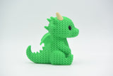 Petit dragon façon tricot sur une bibliothèque en bois près de livres et d'une plante, intérieur chaleureux