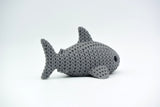 Requin tricoté décoratif sur une étagère en bois à côté de livres et de petites plantes dans un intérieur scandinave