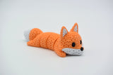 Renard tricoté articulé allongé sur une surface blanche, corps souple