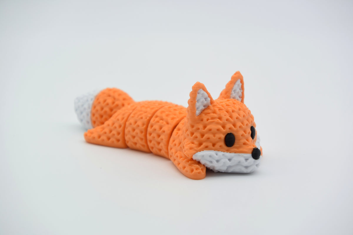 Renard tricoté articulé allongé sur une surface blanche, corps souple