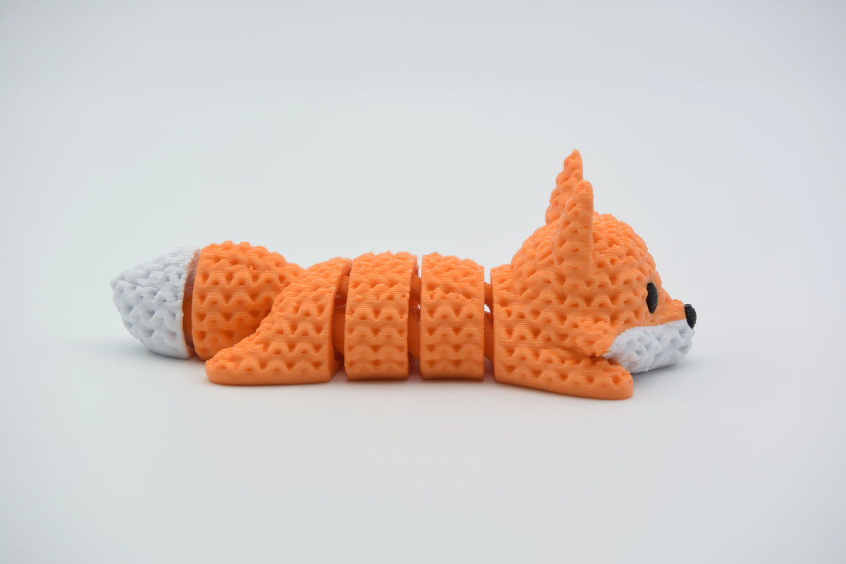 Renard tricoté articulé allongé sur une surface blanche, corps souple