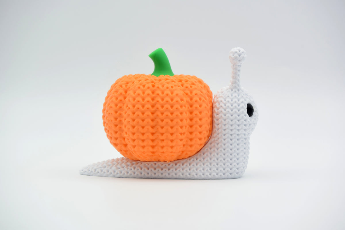 Escargot citrouille tricoté en décoration d'Halloween sur une étagère en bois avec des feuilles séchées et de petites bougies