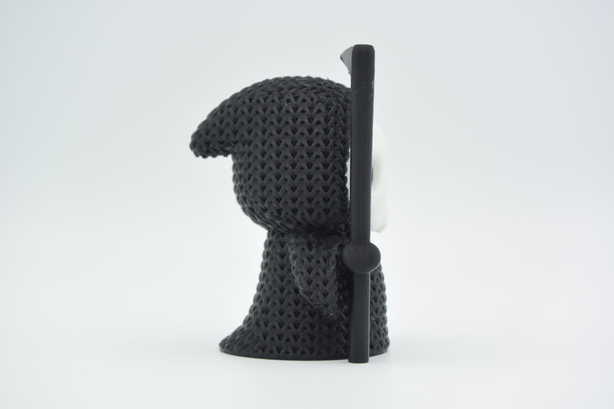 Petite Faucheuse façon tricot pour Halloween sur une étagère en bois sombre près de feuilles d'automne