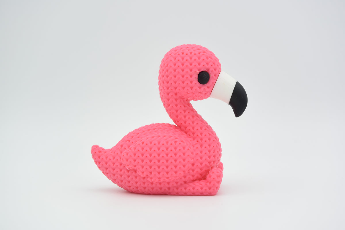 Figurine de flamant rose tricotée sur une étagère en bois à côté d'une petite plante et d'une déco neutre