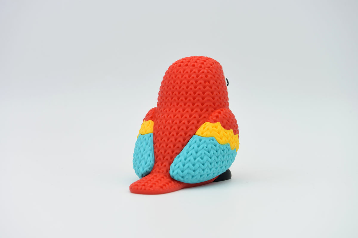 Figurine d'ara rouge tricotée sur une étagère en bois à côté de livres et d'une petite plante